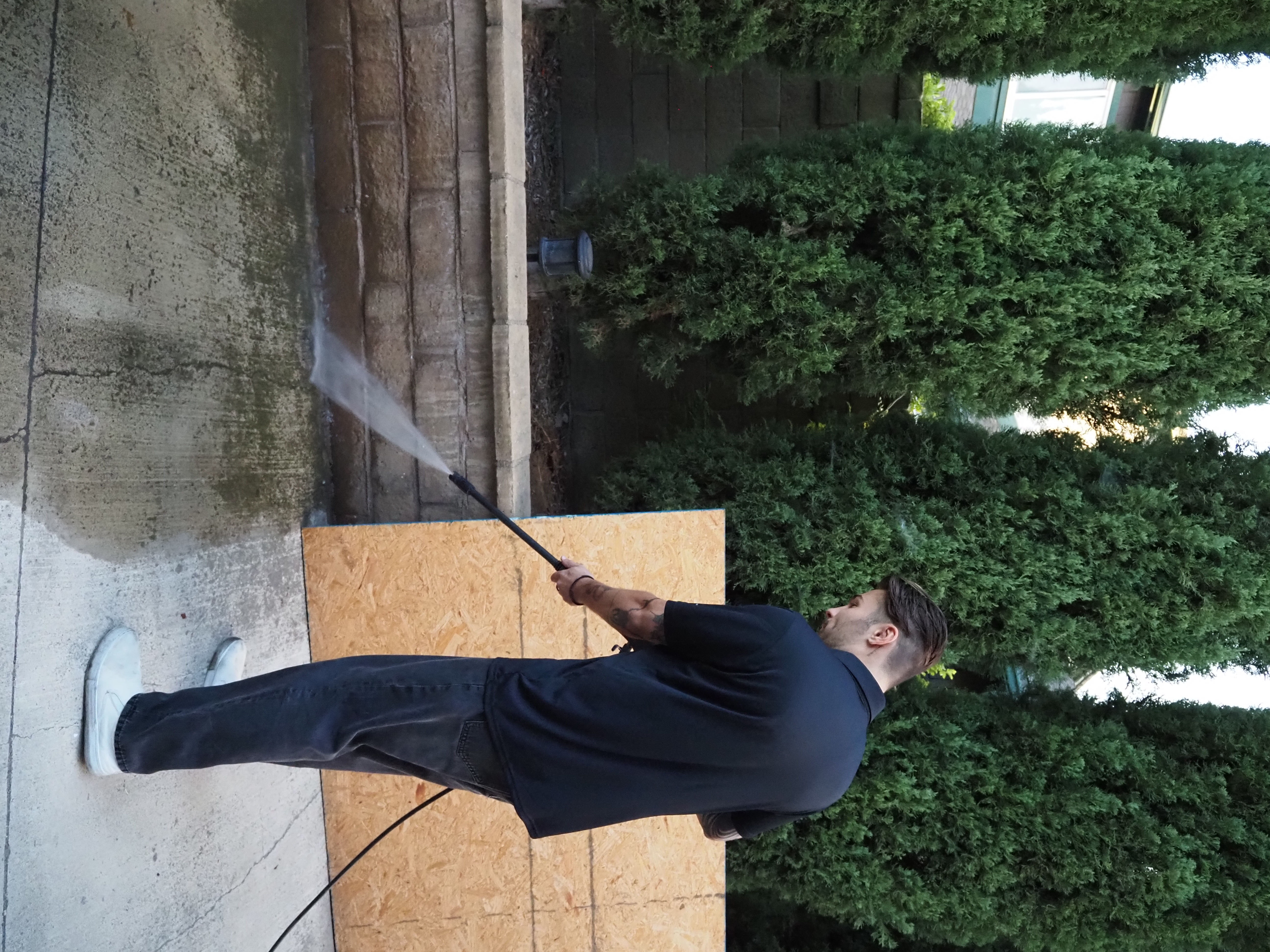 Dylan pressure washing concrete along a retaining wall